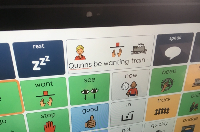 Photo of a eye gaze computer grid screen with the words 'Quinns be wanting train' selected